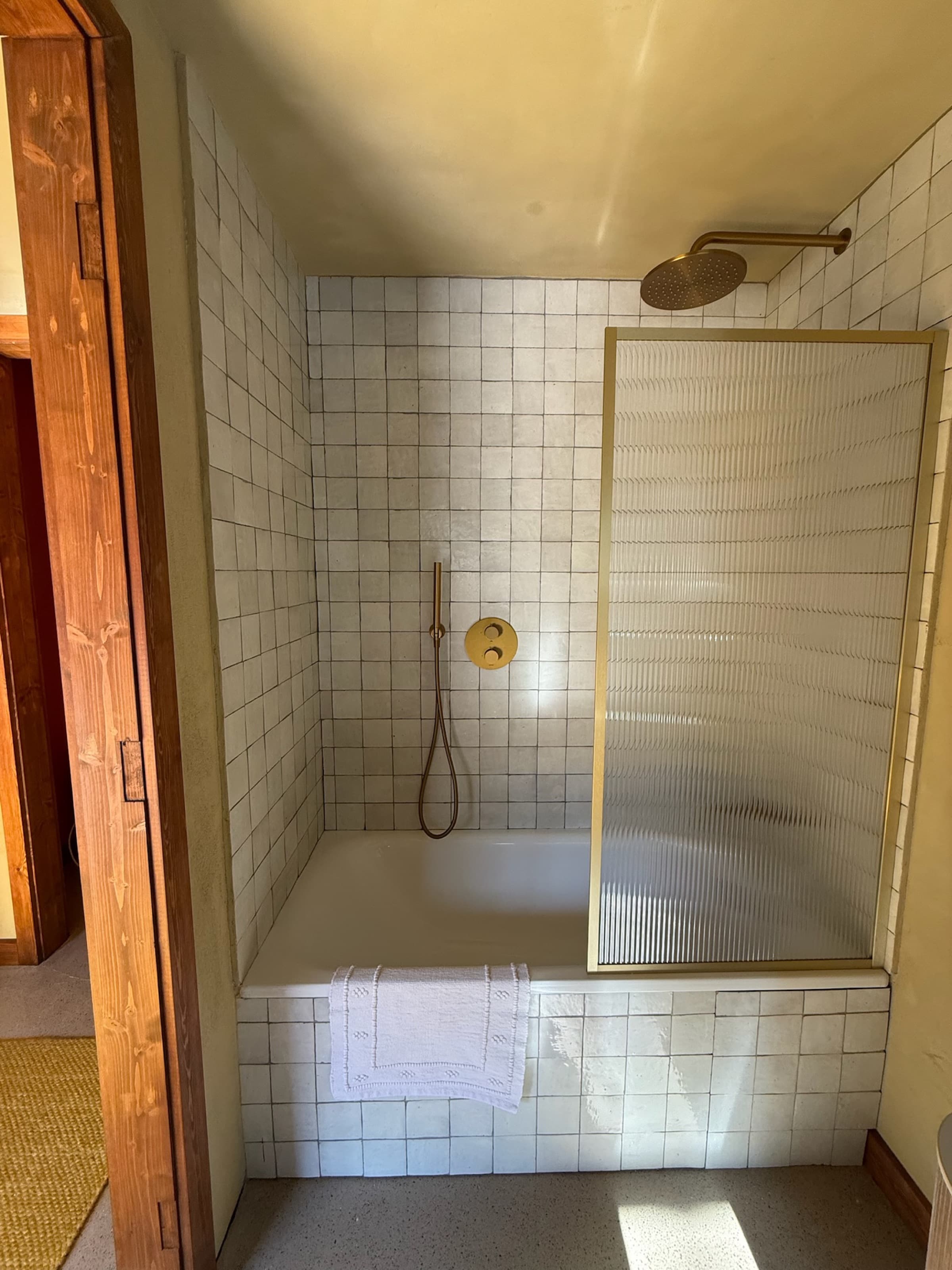 White-tile ensuite with brass rainfall shower and ribbed-glass screen