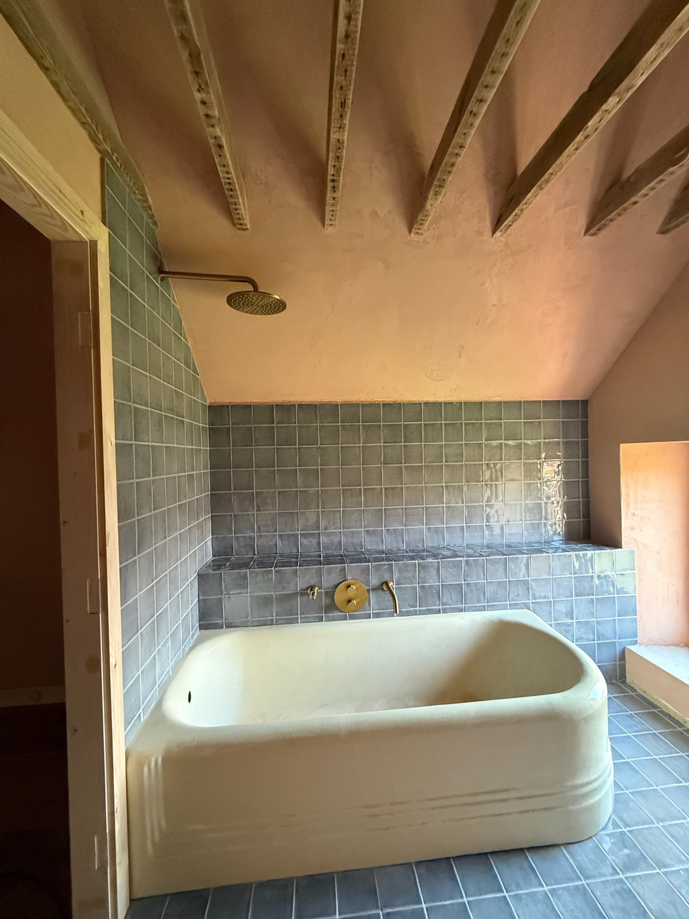 Sculptural freestanding stone bath under vaulted beams, green tile, brass fittings